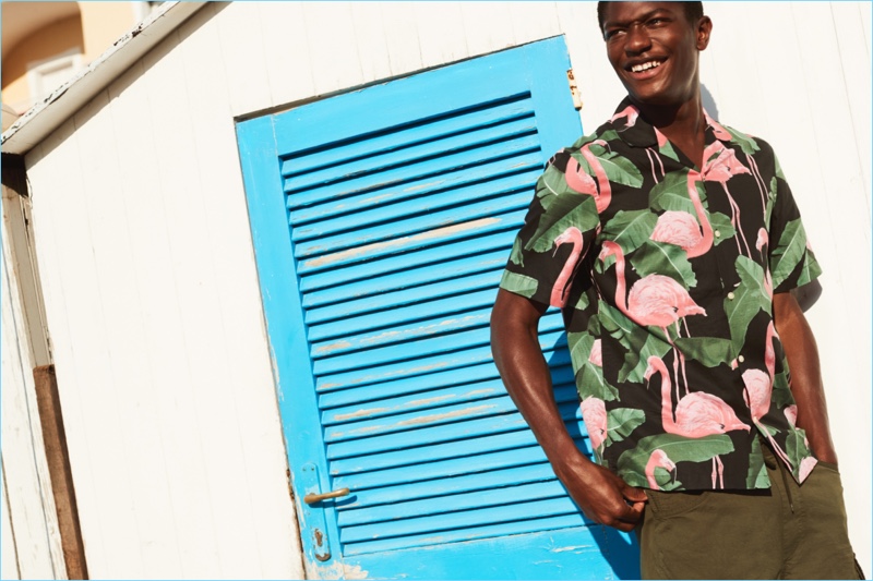 Hamid Onifade reunites with H&M. He wears a relaxed fit flamingo print shirt with cargo shorts.