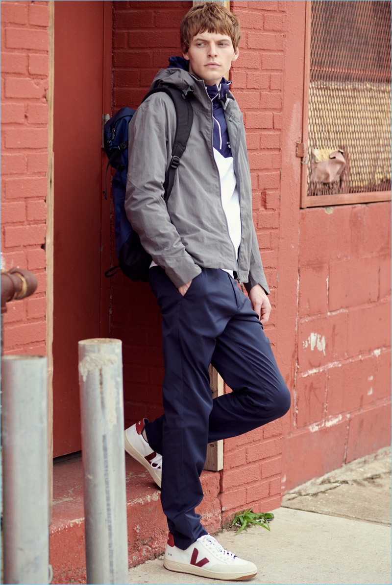 Embracing sporty style, John Hein wears a Vince pima cotton tee, POLO Ralph Lauren anorak, and Arc'Teryx Veilance Isogon jacket. The model also rocks Theory trousers, Veja sneakers, and an Arc-Teryx Brize 25 backpack.