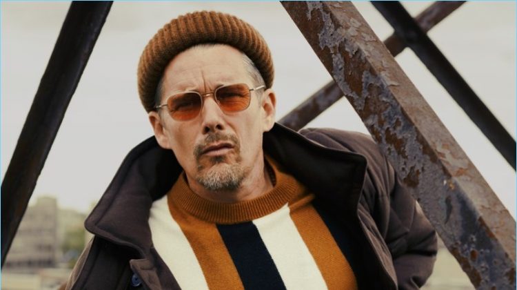 A cool vision, Ethan Hawke wears a BOSS coat, pants, and beanie. Hawke also rocks a Sandro sweater and Garrett Leight sunglasses.