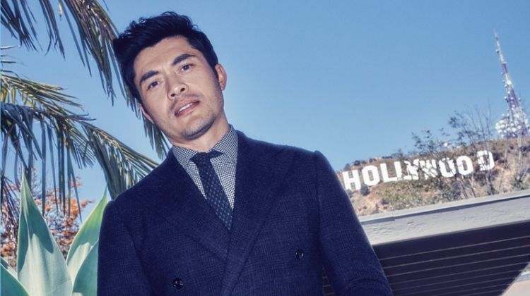 Henry Golding wears a sharp suit, shirt, and tie by Ralph Lauren.