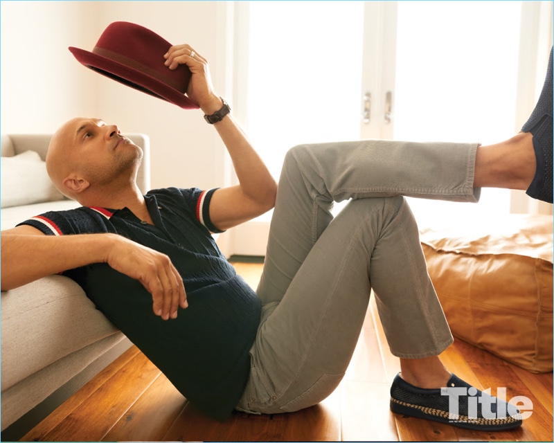 Relaxing, Keegan-Michael Key dons a Burberry polo, Citizens of Humanity pants, Baldinini sneakers, and a Goorin Bros. hat.