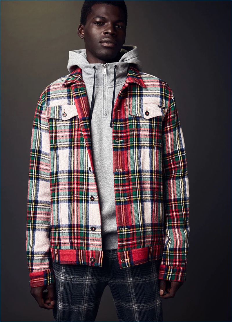 Model Evandro Laurens sports a hoodie with a tartan trucker jacket and trousers by Scotch & Soda.