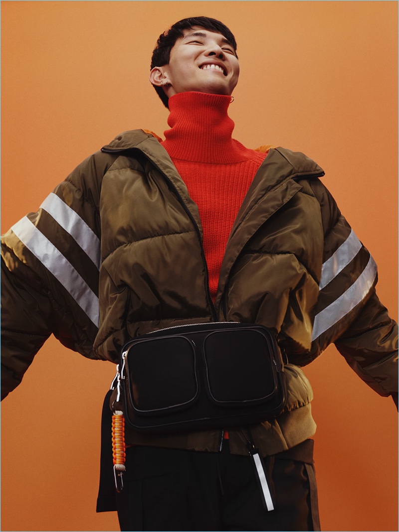 All smiles, Jeon June wears an oversized puffer jacket with a red turtleneck sweater and belt bag from Zara Man.