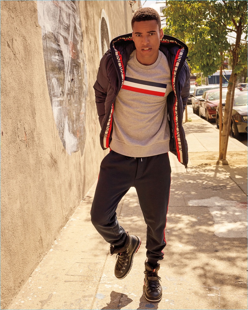 Malik Lindo sports a Moncler graphic sweatshirt, puffer jacket, side-stripe pants, and hiking boots.