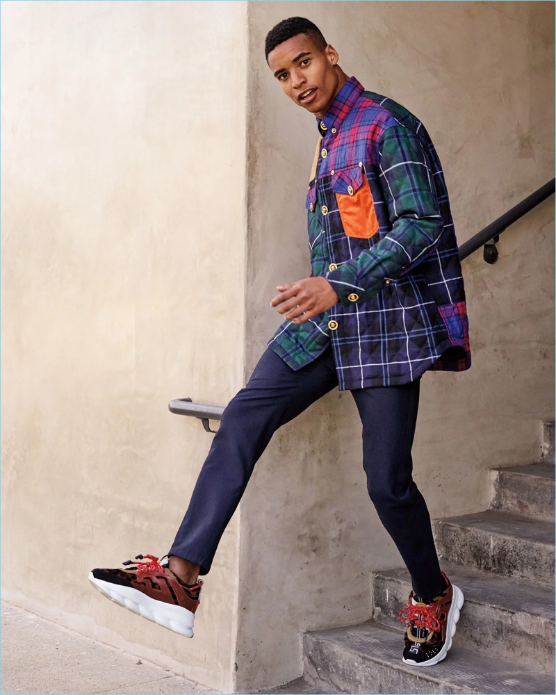 Stepping out in Versace, Malik Lindo wears an oversized plaid shirt jacket, straight-leg pants, and sneakers.