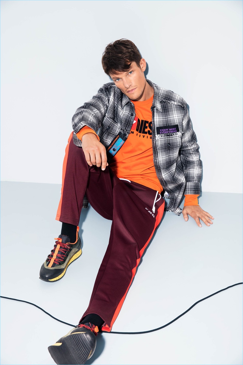 Danny Beauchamp wears joggers with a plaid shirt, long-sleeve tee, and shoes by Diesel.