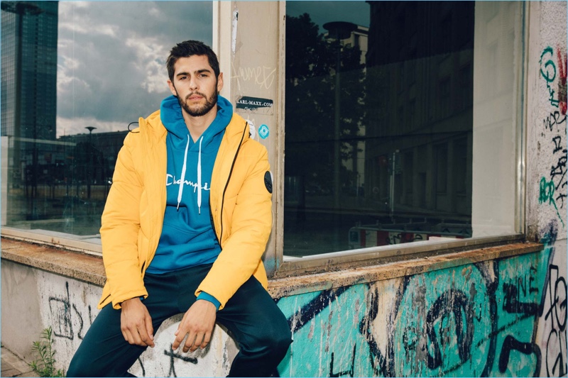 Embracing a pop of color, René Grincourt models a yellow Jack & Jones jacket with a Champion hoodie, Jack & Jones joggers, and Adidas sneakers.