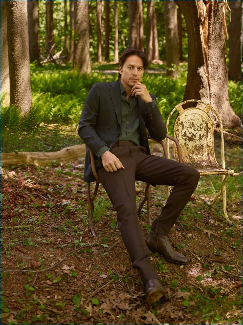 Sitting for a portrait, Cary Fukunaga wears a Kiton sports jacket, Salvatore Ferragamo shirt, BOSS pants, and Tom Ford boots.