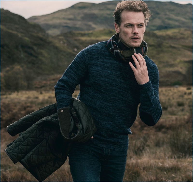 Appearing in a new photo, Sam Heughan dons a lambswool sweater from his Barbour collaboration.