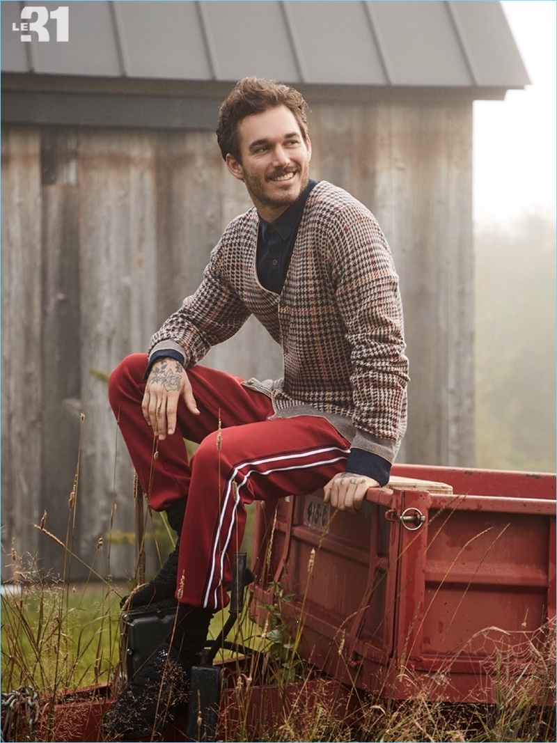 All smiles, David Alexander Flinn wears a LE 31 houndstooth cardigan, chambray jean shirt, and striped athletic pants.