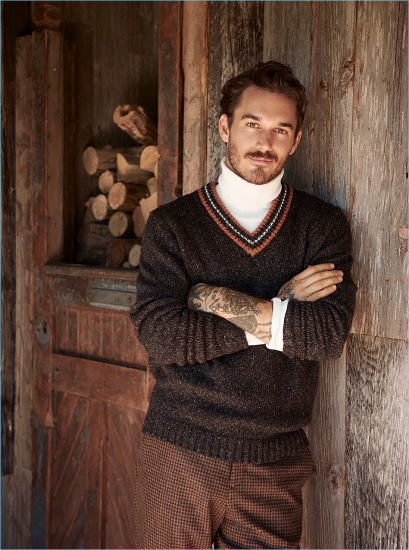 Embracing preppy style, David Alexander Flinn dons a LE 31 retro varsity sweater, turtleneck sweater, and gingham check trousers.