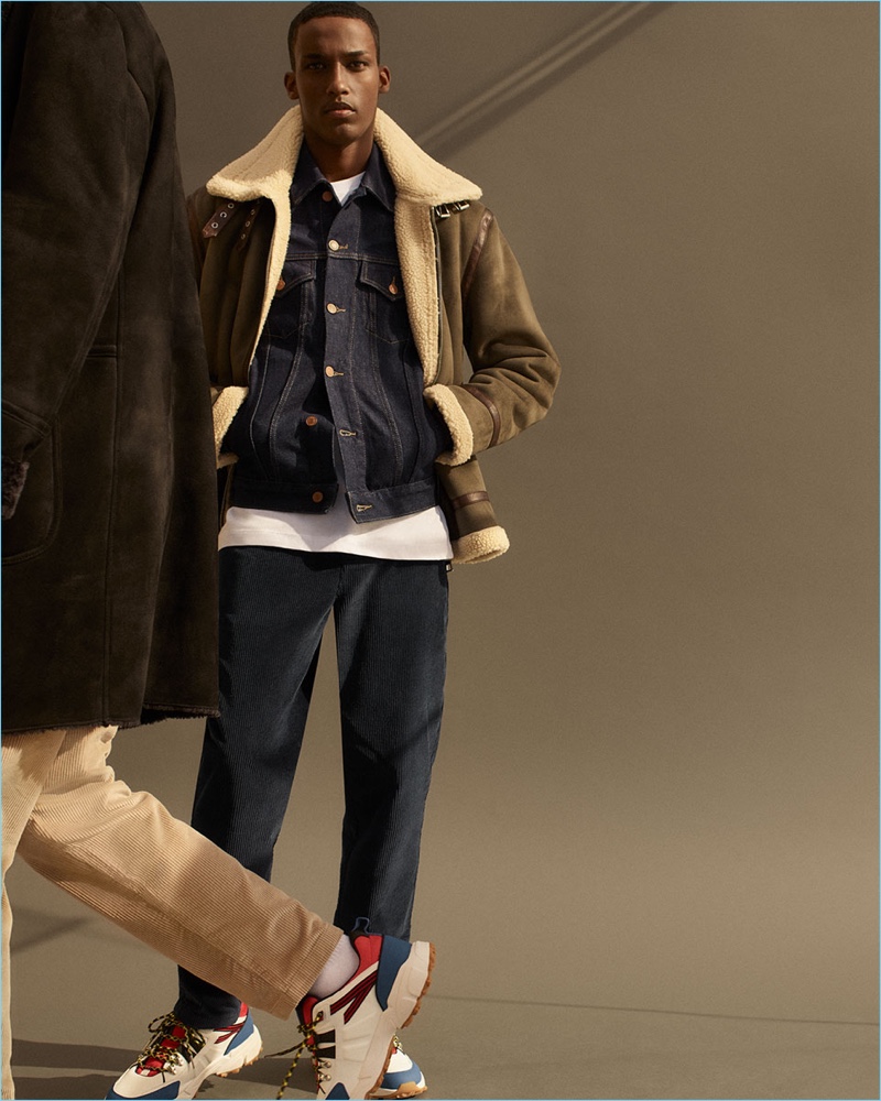 Connecting with Zara, Mahad Musse sports a khaki aviator jacket, raw denim jacket, corduroy trousers, and sneakers.