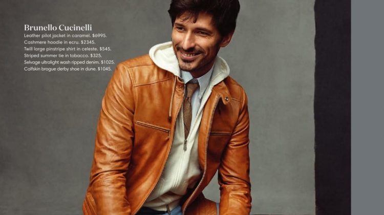 All smiles, Andres Velencoso dons a Brunello Cucinelli caramel leather jacket, cashmere hoodie, pinstripe shirt, striped tie, ripped jeans, and brogue derby shoes.