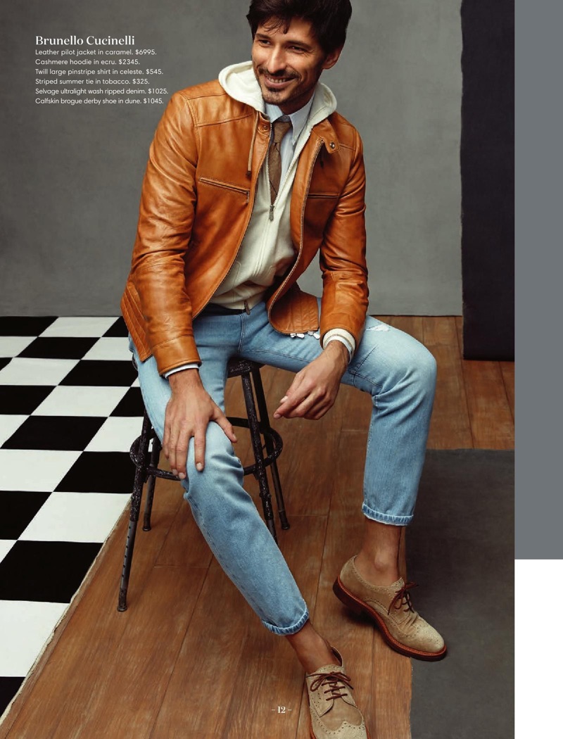 All smiles, Andres Velencoso dons a Brunello Cucinelli caramel leather jacket, cashmere hoodie, pinstripe shirt, striped tie, ripped jeans, and brogue derby shoes.