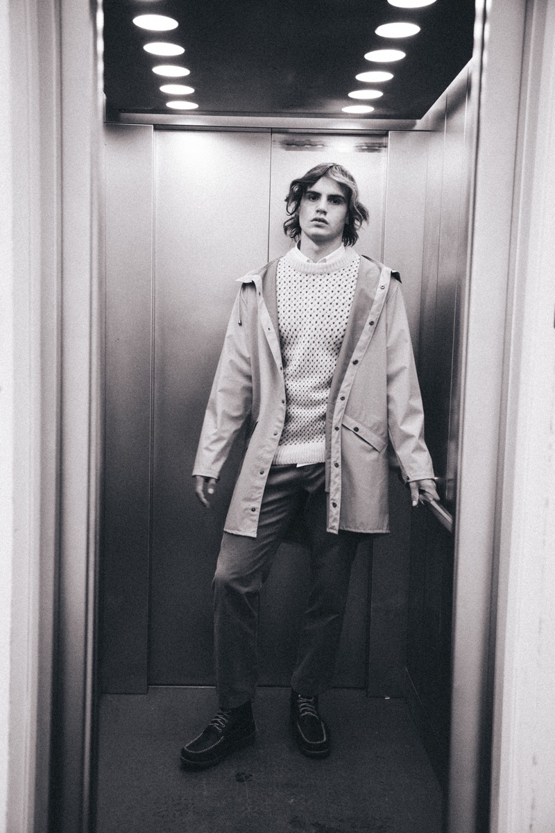 Kit wears raincoat Rains, sweater You Must Create, trousers Norse Projects, shirt Remus Uomo, and boots GH Bass & Co.