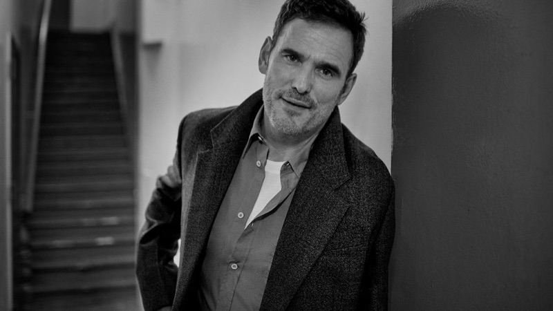 Appearing in a black and white photo, Matt Dillon wears a Prada coat, Maison Margiela shirt, and Berluti t-shirt.