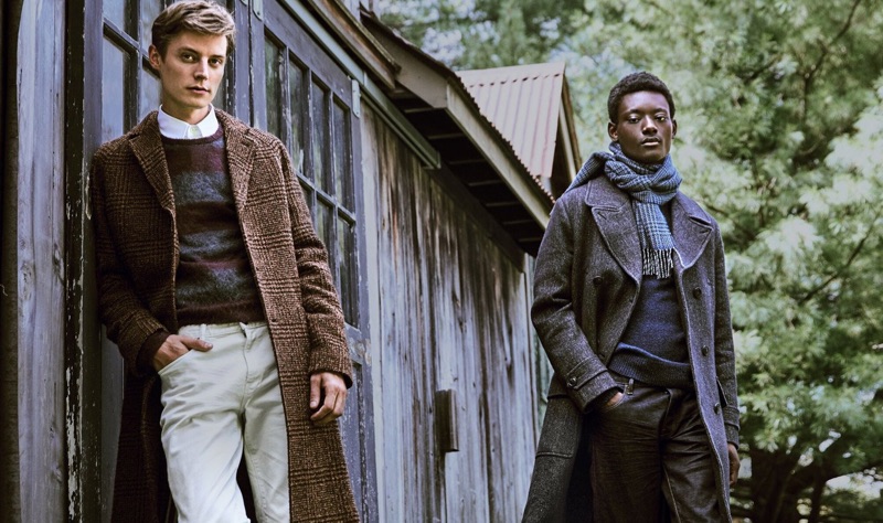 Models Janis Ancens and Youssouf Bamba prepare for the holidays with Todd Snyder. Left to Right: Janis dons an Italian wool bouclé glen plaid topcoat in brown. He also sports an Italian brushed wool rugby striped sweater and 5-pocket stretch pants. Meanwhile, Youssouf models a Todd Snyder Italian wool twill officer coat and navy sweater with a Drake's wool glen check scarf.