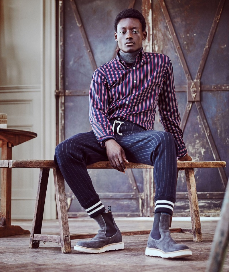 Mixing prints, Youssouf Bamba wears Todd Snyder + Champion wide stripe sweatpants with a Hamilton + Todd Snyder stripe shirt. He also rocks a marled grey chunky cashmere turtleneck and Tricker's Chelsea boots.