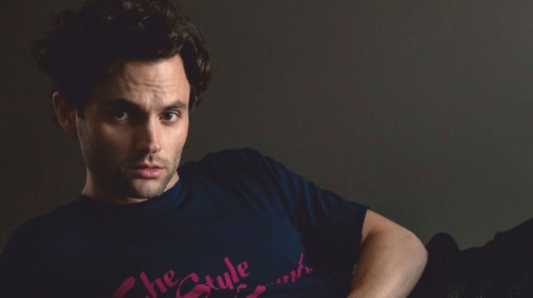 Posing for a studio photo, Penn Badgley wears an Opening Ceremony t-shirt, Bally trousers, and COS shoes.