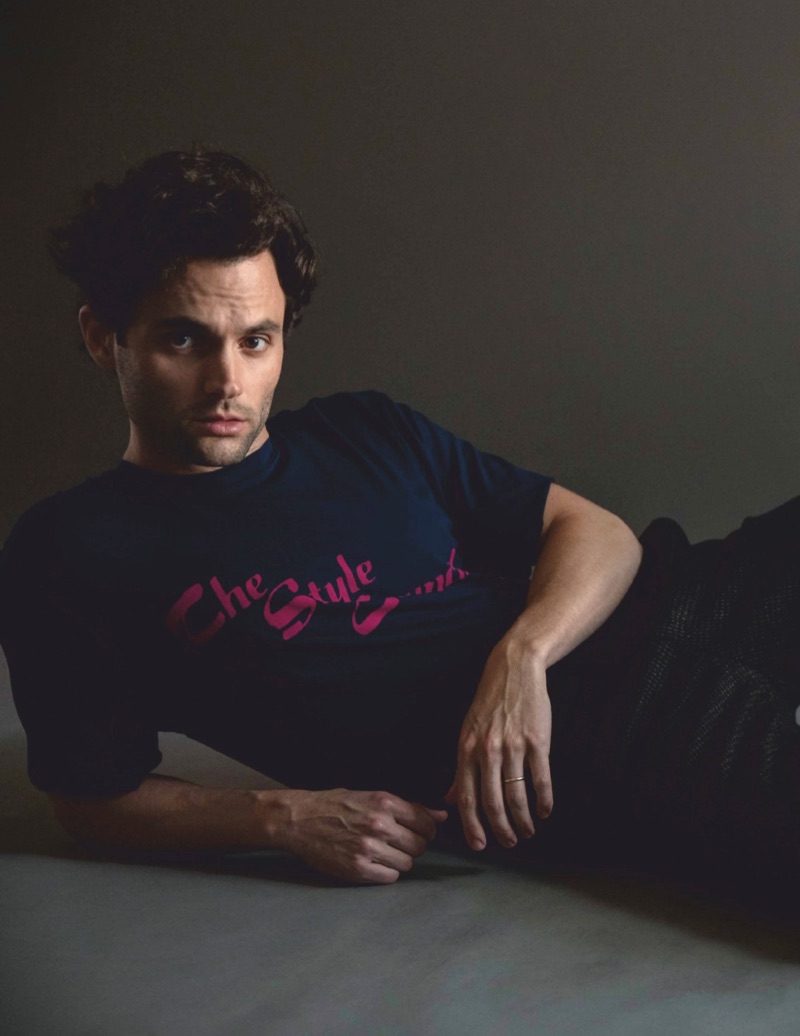 Posing for a studio photo, Penn Badgley wears an Opening Ceremony t-shirt, Bally trousers, and COS shoes.