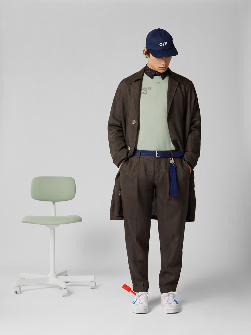 Donning brown, Louis Baines wears an Off-White oversized trench coat and linen trousers. He also sports an Off-White baseball cap, leather belt, sneakers, and t-shirt.