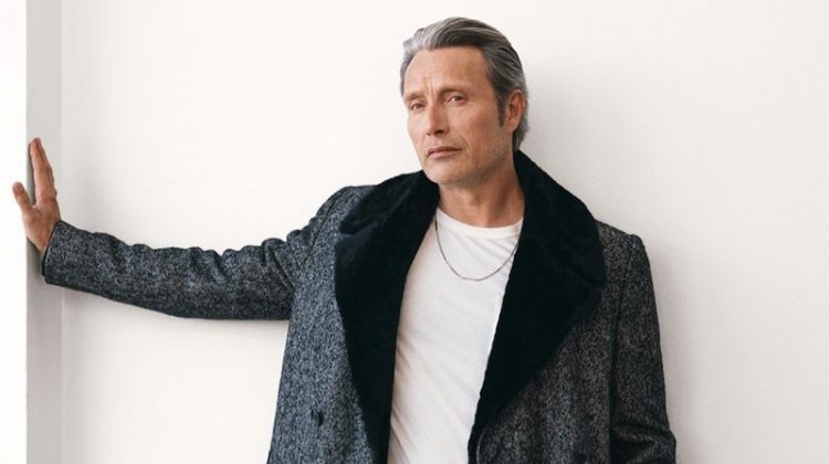 Connecting with Mr Porter, Mads Mikkelsen sports a Dunhill herringbone coat, Tom Ford t-shirt, Berluti trousers, Loro Piana suede belt, and Saint Laurent necklace.