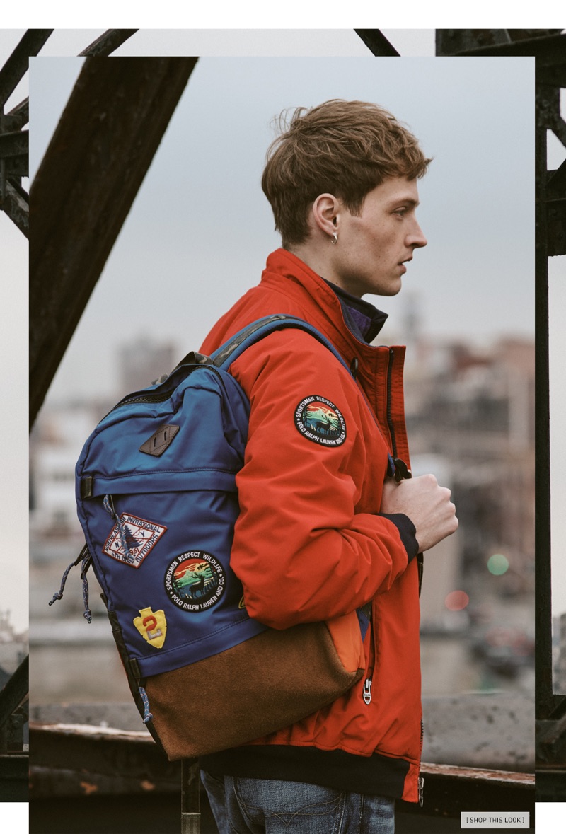 Delivering a side profile, Dane Bell sports a POLO Ralph Lauren jacket, jeans, and a backpack.