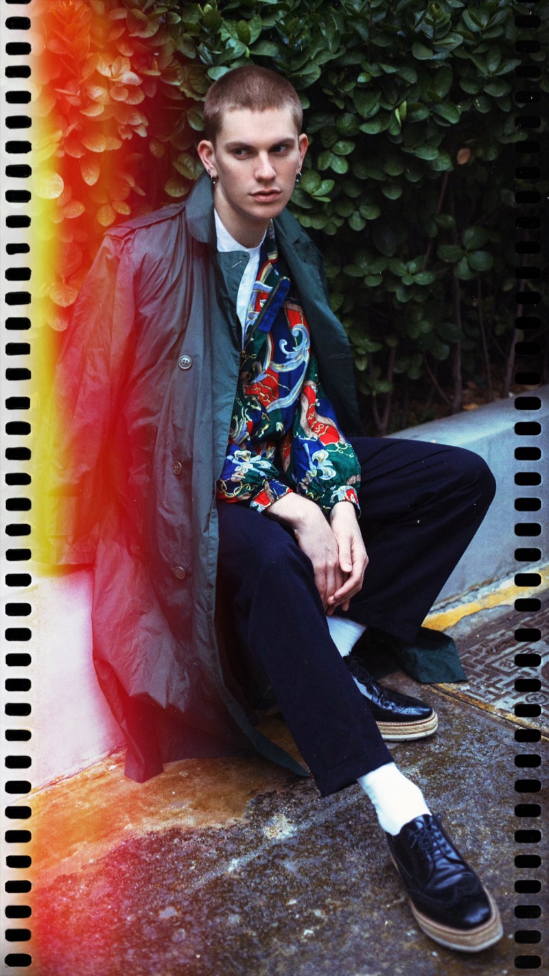Captured outdoors, Alexander Morel wears a vintage Fuda International jacket with Prada pants. He also sports a vintage trench, Ralph Lauren shirt, and Prada leather shoes.