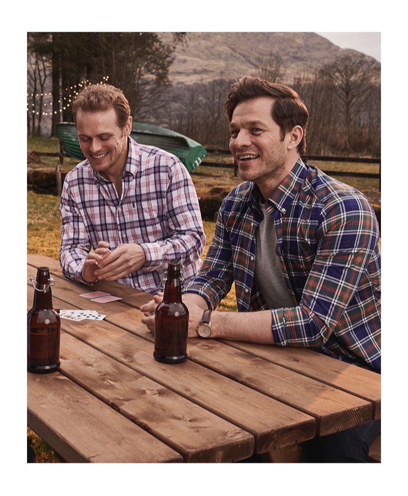 Sporting plaid shirts by Barbour, Sam Heughan and Paul Sculfor sit down for drinks.