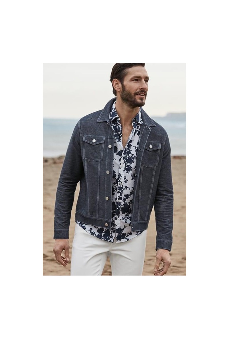 A smart vision, Parker Gregory dons a Michael Kors stretch denim trucker jacket, floral print shirt, and white slim-fit jeans.