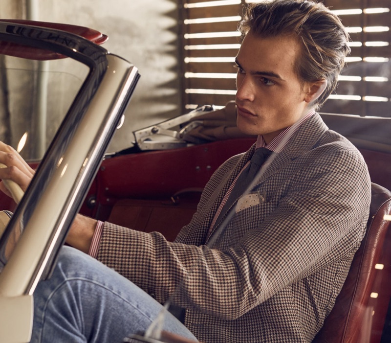 Sitting in a vintage car, Parker van Noord wears a suit jacket with a pair of denim jeans.