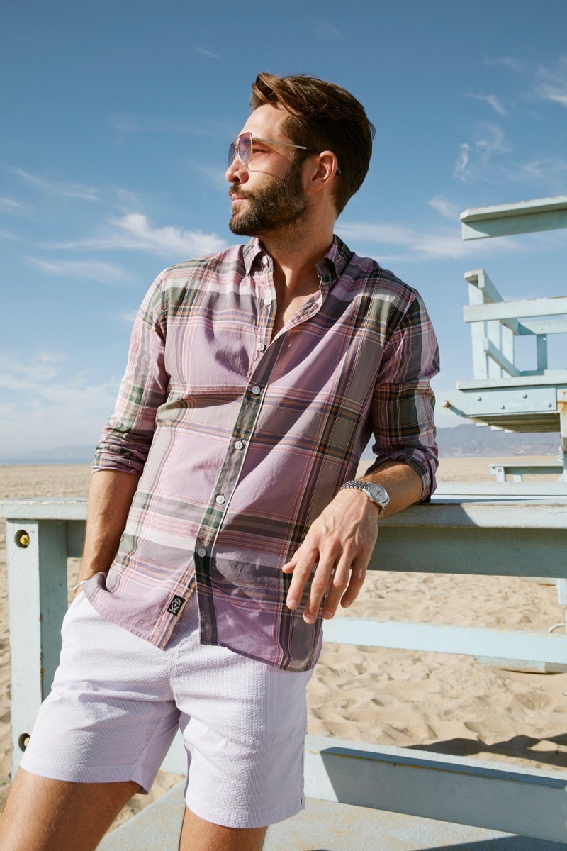 Model John Halls wears a Todd Snyder lightweight button-down purple Madras shirt and 7" weekend stretch shorts in lavender.