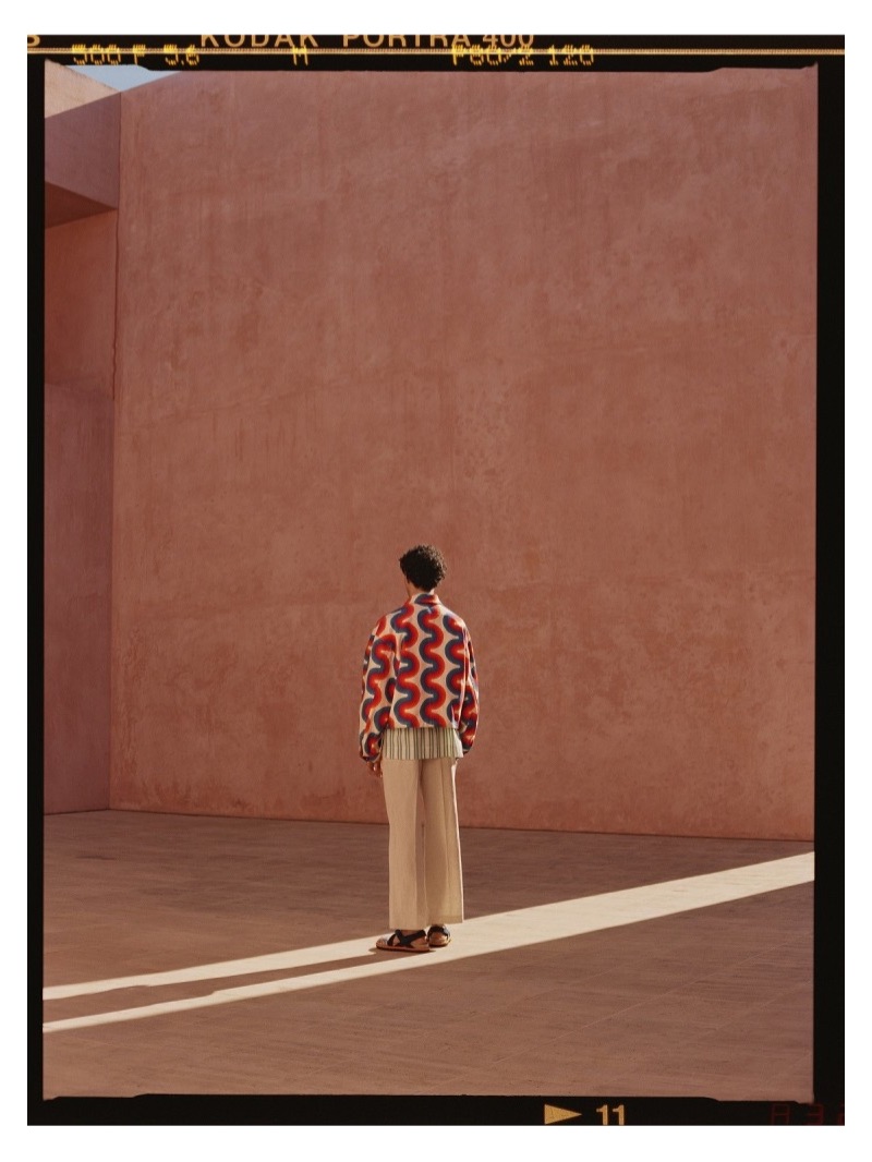 Making a colorful statement, Dylan wears a Dries Van Noten printed denim jacket, Acne Studios striped shirt, and Jacquemus pleated trousers. Dries Van Noten sandals complete Dylan's look.