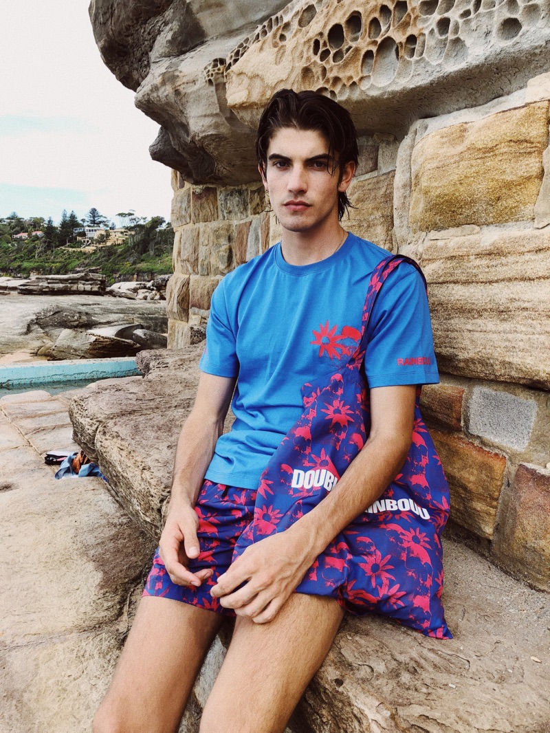 Connecting with East Dane, Cal Fernie wears a Double Rainbouu t-shirt and swim shorts. He also takes hold of the brand's Hawaiian print tote.