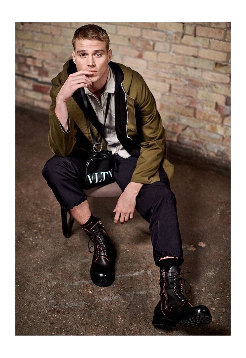 Embracing military-inspired style, Matthew Noszka dons an AMIRI parka, Stone Island overshirt jacket, Junya Watanabe cargo pants, a Valentino Garavani VLTN leather pouch, and Rick Owens leather army boots.