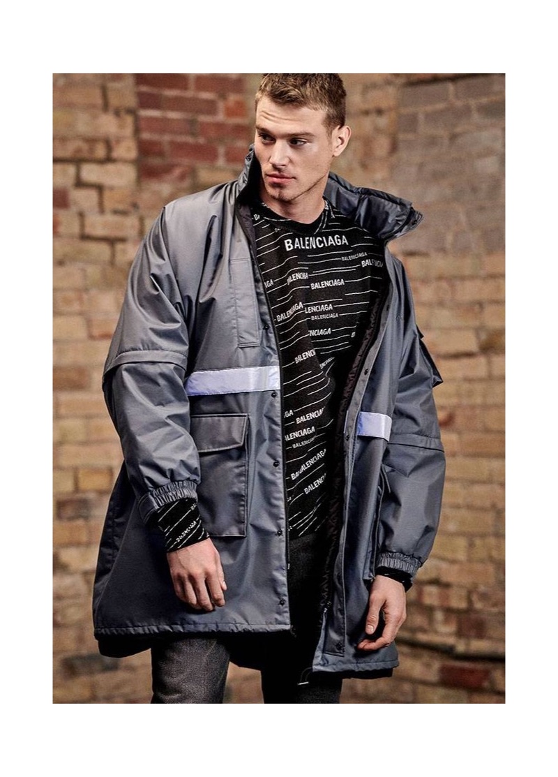 Model Matthew Noszka rocks a Balenciaga nylon parka, logo jacquard sweater, and bootcut jeans.
