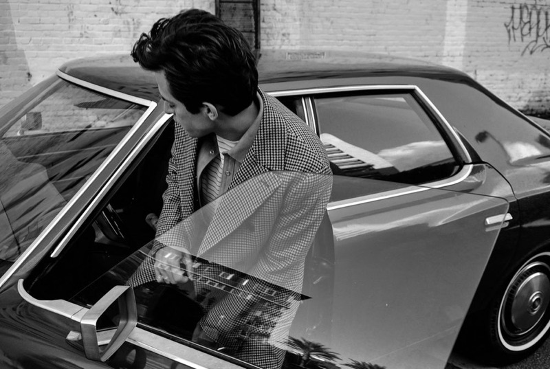 Getting into a vintage car, Mark Ronson wears a Brunello Cucinelli double-breasted houndstooth jacket and Neighborhood suede overshirt. He also dons a Handvaerk striped t-shirt and Prada trousers.