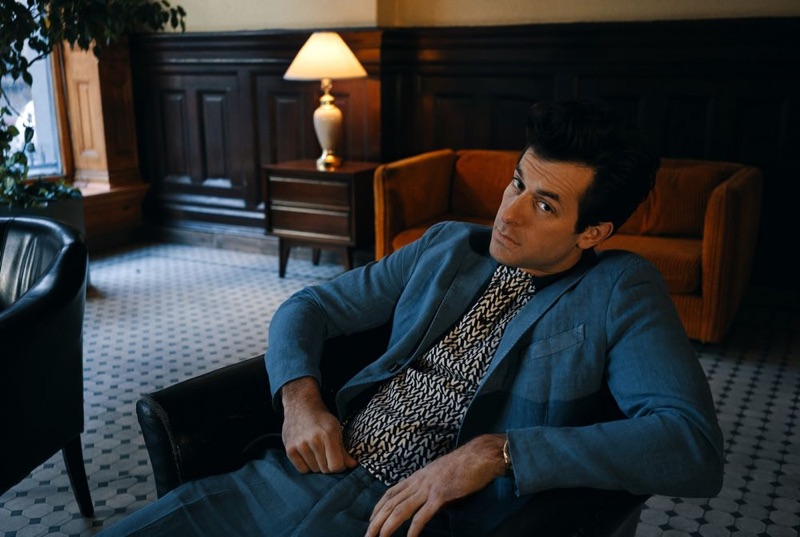 Sitting for a photo, Mark Ronson wears a blue Boglioli suit with a Valentino logo polo shirt.