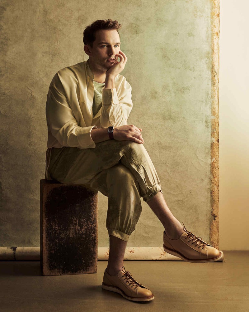 Sitting for a photo, Nicholas Hoult wears a silk Louis Vuitton shirt, Sean Suen ribbed t-shirt, Giorgio Armani trousers, and Tricker's shoes.