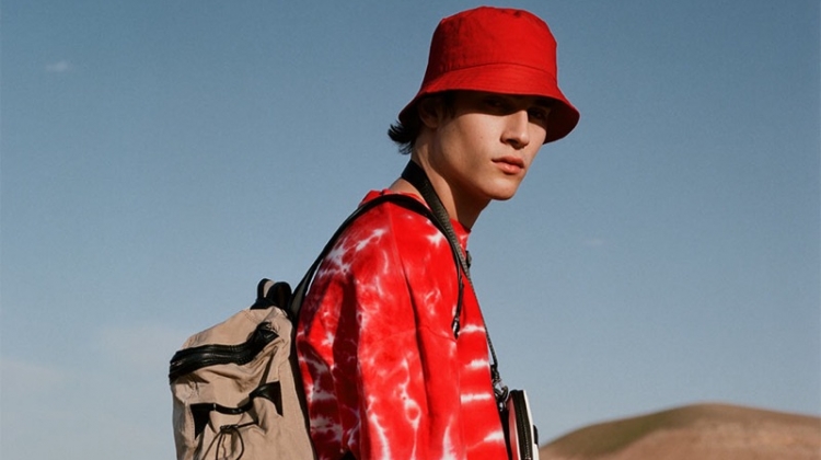 Rocking red, Liam Kelly sports a tie-dye print t-shirt with a bucket hat and white pants by Reserved.