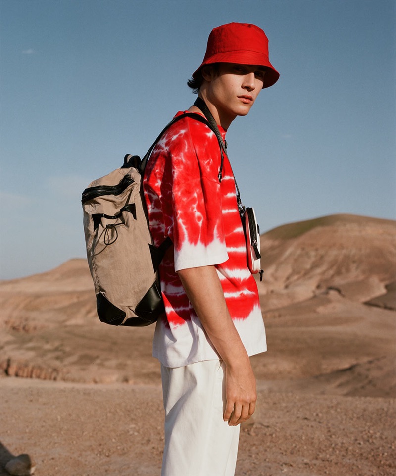 Rocking red, Liam Kelly sports a tie-dye print t-shirt with a bucket hat and white pants by Reserved.