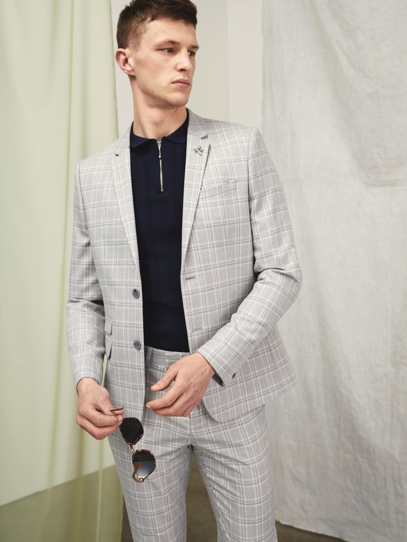 Dressed to impress, Jack Buchanan dons a grey check River Island suit with a half-zipper polo.