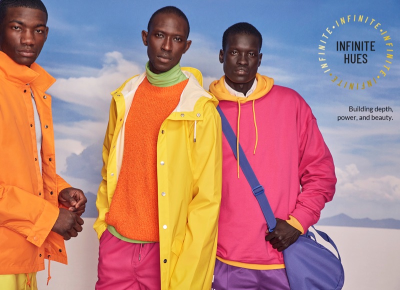 Models Valentine Rontez, Armando Cabral, and Monywiir Deng Dharjang sport brightly colored fashions for Simons. Left to Right: Valentine wears an Alpha Industries orange coach jacket with a LE 31 knit polo and Calvin Klein swim trunks. Armando sports a yellow Rains trench coat, orange LE 31 sweater and pink shorts. Monywiir rocks a yellow DJAB hoodie and pink sweatshirt with purple Kappa joggers. He also takes hold of a blue Herschel weekend bag.