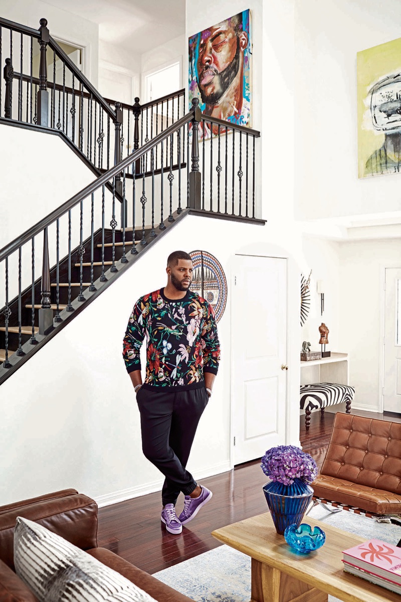 Posing in his home, Winston Duke wears a Gucci sweater, Dolce & Gabbana joggers, and Christian Louboutin sneakers. A David Yurman bracelet and TAG Heuer watch completes his look.