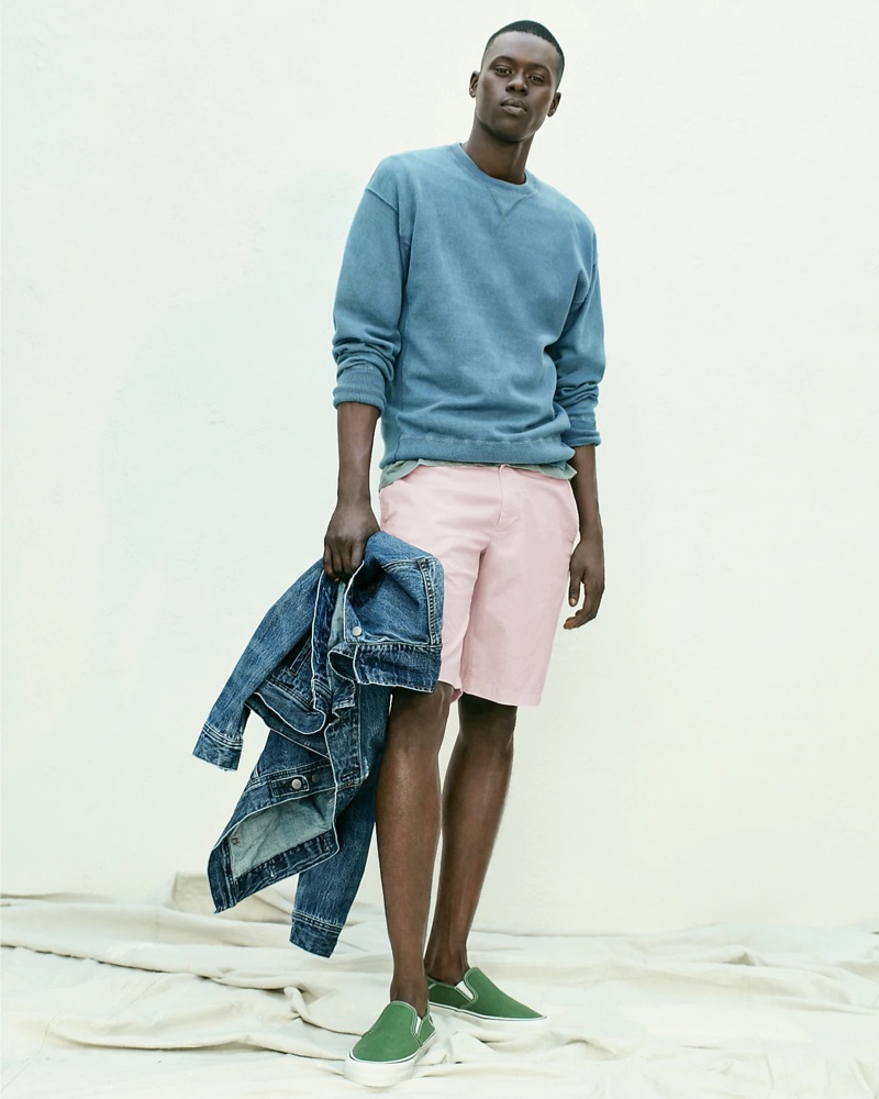 Casual for summer, Alpha Dia sports a J.Crew classic denim jacket with a blue side-panel crewneck sweatshirt. Alpha also wears pink shorts and green Vans slip-on sneakers.