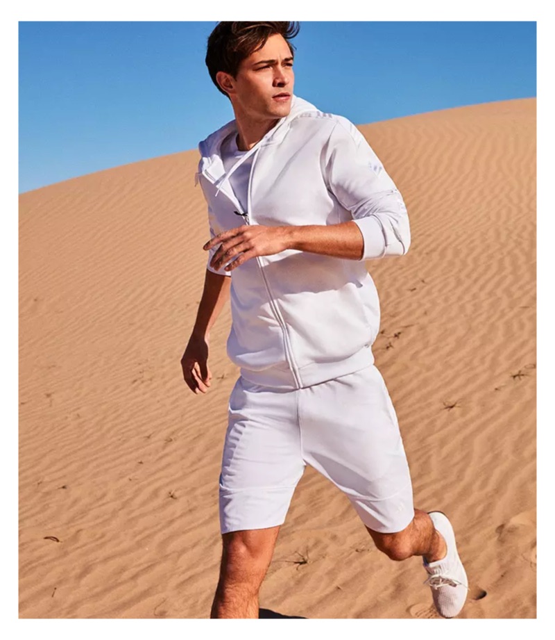 Embracing sporty style, Francisco Lachowski wears all white in a hoodie, tee, shorts, and knit sneakers.