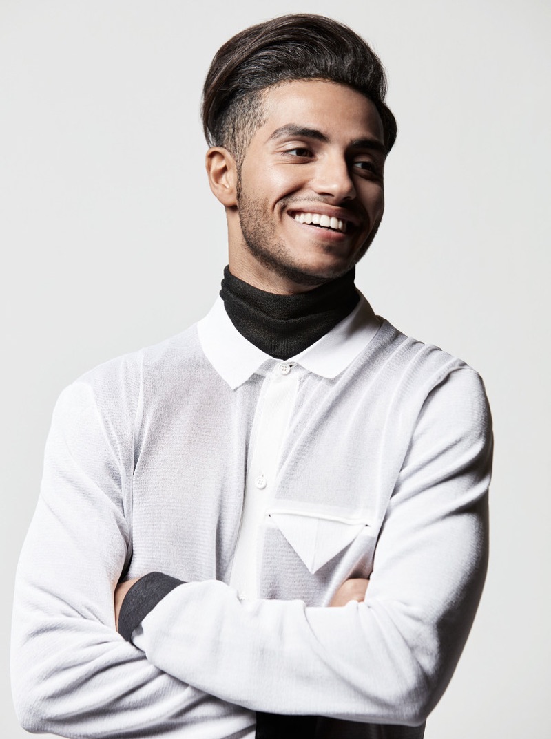 All smiles, Mena Massoud wears a turtleneck sweater and shirt from Bottega Veneta.