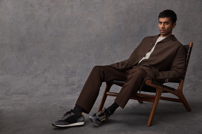 Embracing a rich brown hue, Nikesh Patel wears a Prada coat, trousers, and Milano 70 nylon and suede sneakers with a Beams Plus mélange mohair-blend sweater.