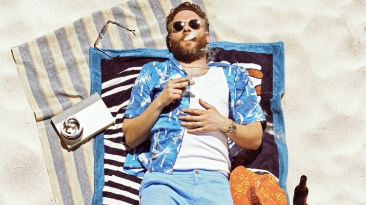 Relaxing on an Hermès beach towel, Seth Rogen wears a Dior Men shirt, Calvin Klein tank, POLO Ralph Lauren shorts, Birkenstock sandals, and Garrett Leight sunglasses.
