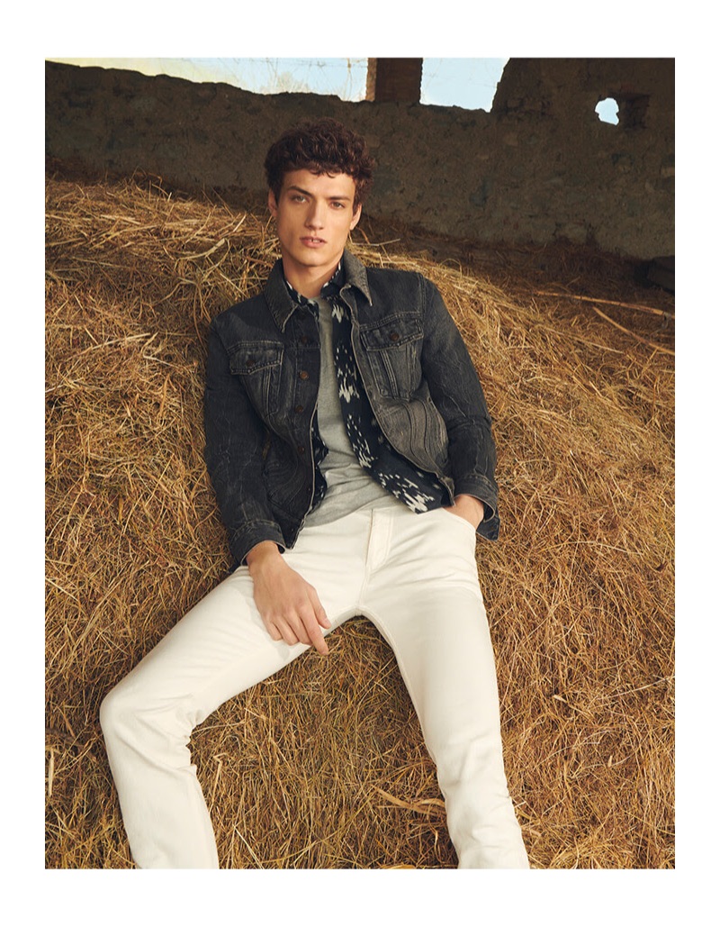 Laying in the hay, Serge Rigvava wears a Saint Laurent denim jacket with white jeans by Burberry.